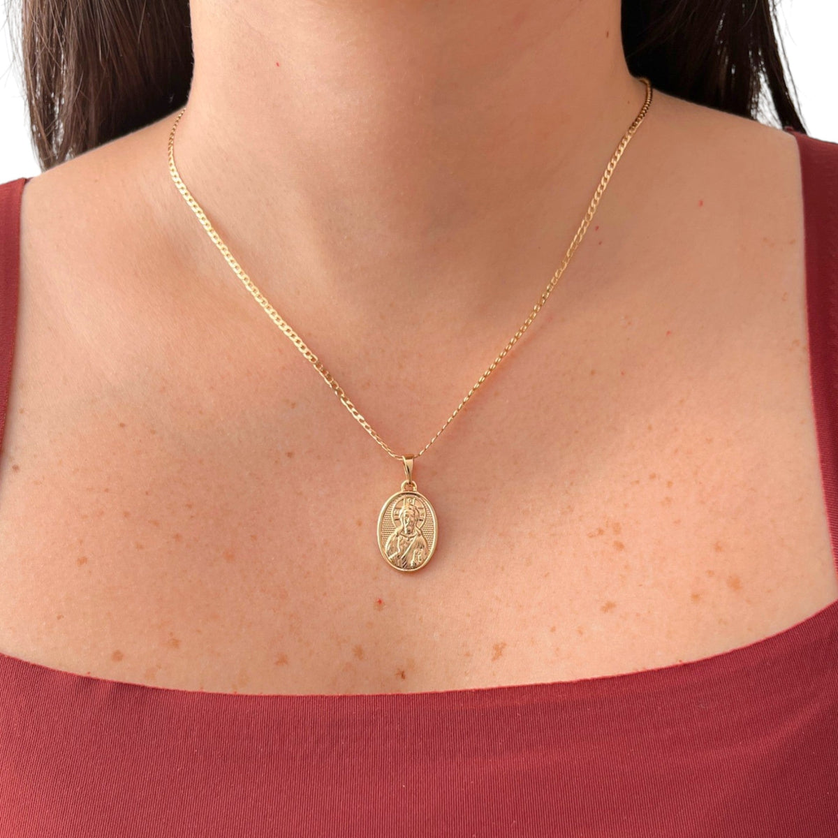 Cadena de tejido Grumet en acabado dorado, acompañada por un dije en forma de medalla ovalada. En el centro destaca la imagen en relieve de San Judas Tadeo sobre un fondo texturizado, enmarcada por un borde de perfil liso.