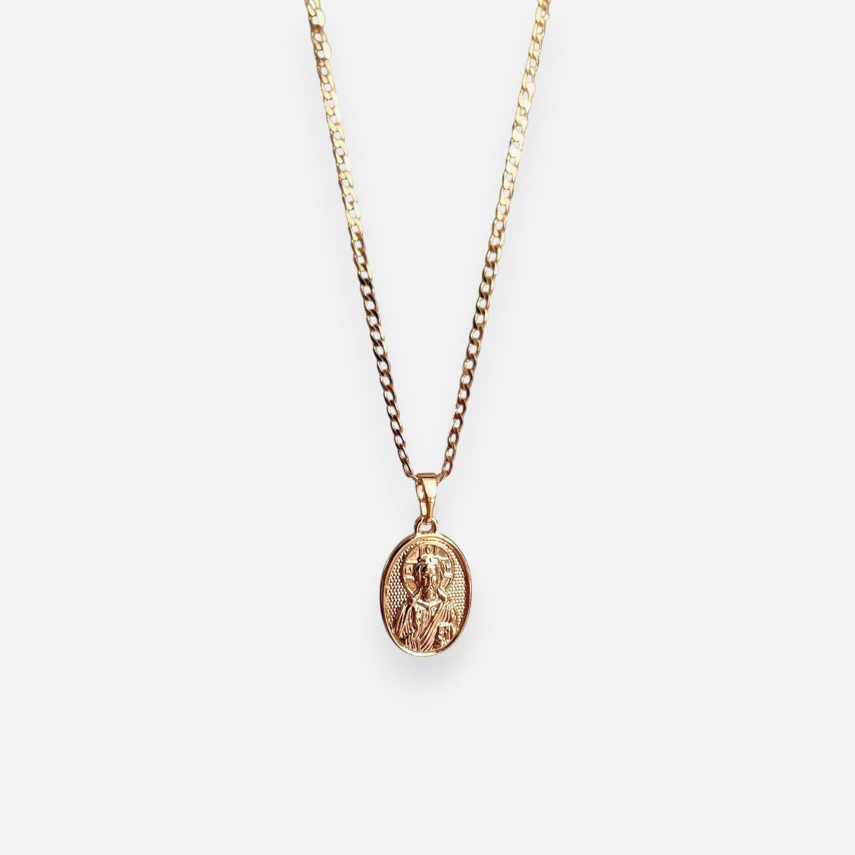 Cadena de tejido Grumet en acabado dorado, acompañada por un dije en forma de medalla ovalada. En el centro destaca la imagen en relieve de San Judas Tadeo sobre un fondo texturizado, enmarcada por un borde de perfil liso.