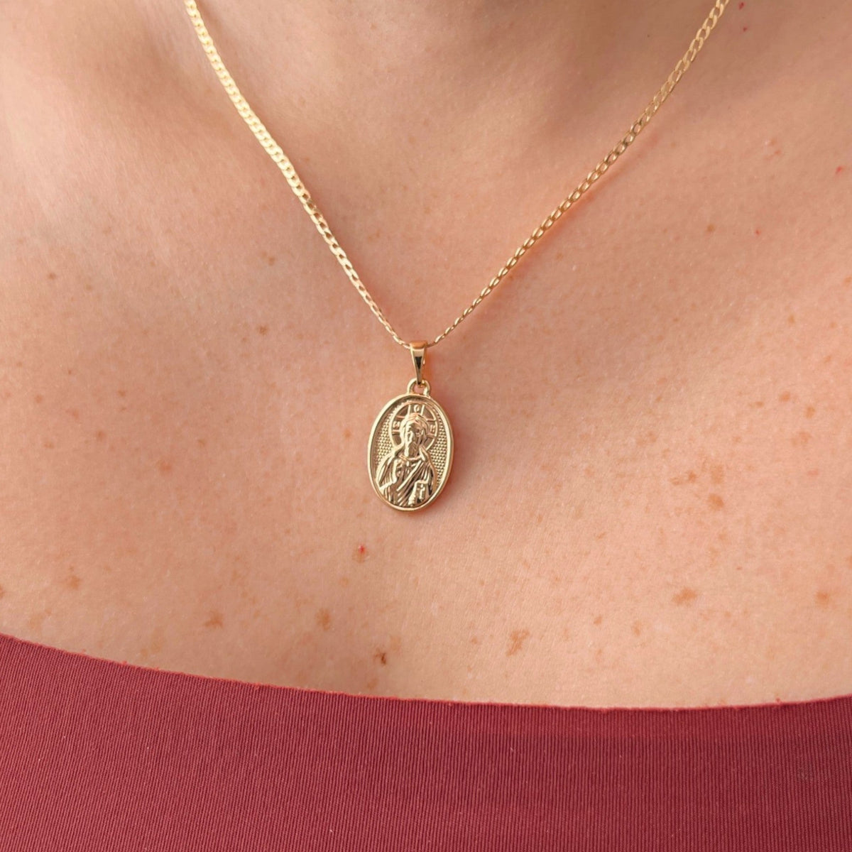 Cadena de tejido Grumet en acabado dorado, acompañada por un dije en forma de medalla ovalada. En el centro destaca la imagen en relieve de San Judas Tadeo sobre un fondo texturizado, enmarcada por un borde de perfil liso.