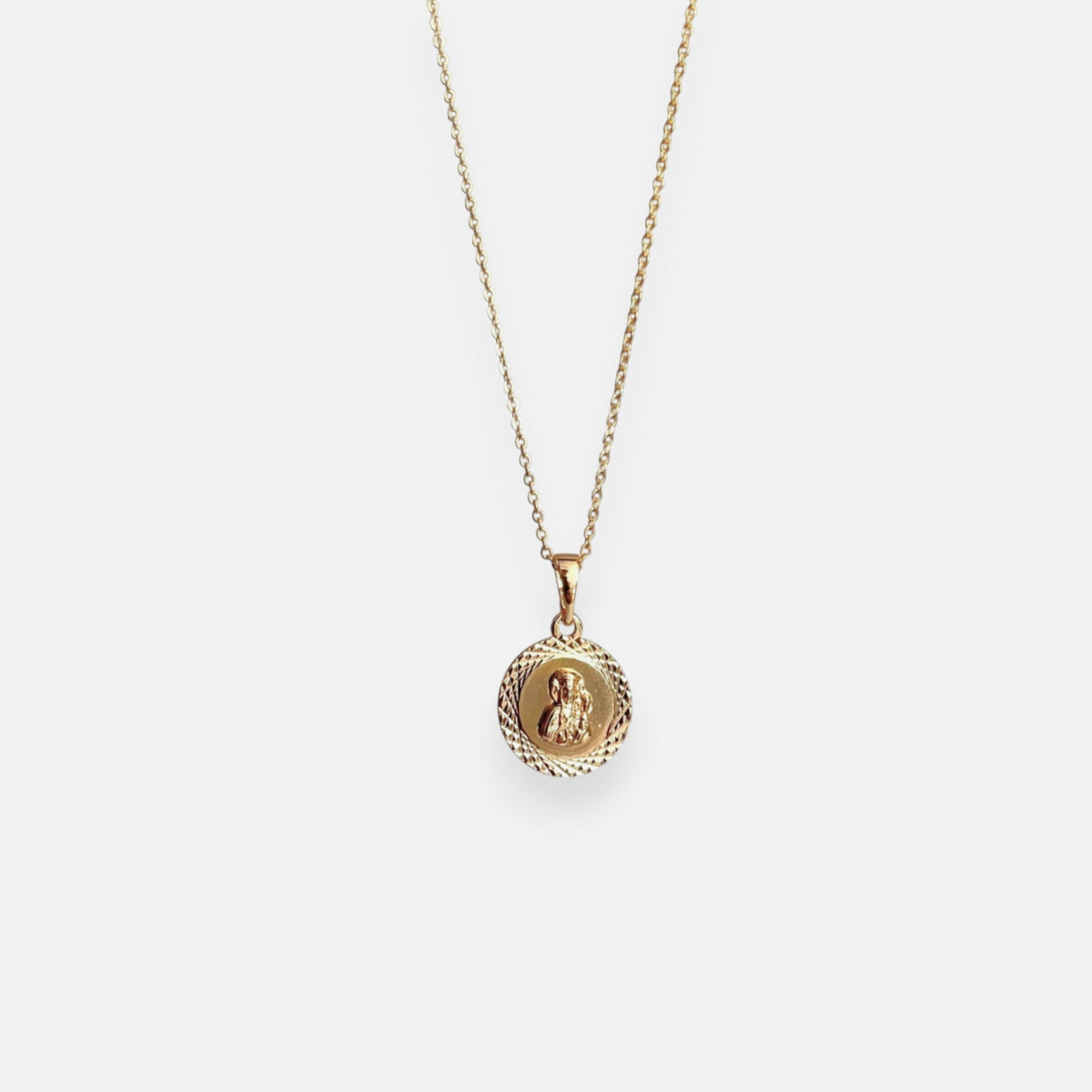 Cadena de tejido Rolo en acabado dorado, acompañada por un dije en forma de medalla circular. En el centro se distingue la figura en relieve de la Virgen del Carmen con el Niño Jesús, enmarcada por un llamativo borde con tallado diamantado o labrado que aporta un brillo especial a la pieza.