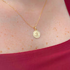 Cadena de tejido Rolo en acabado dorado, acompañada por un dije en forma de medalla circular. En el centro se distingue la figura en relieve de la Virgen del Carmen con el Niño Jesús, enmarcada por un llamativo borde con tallado diamantado o labrado que aporta un brillo especial a la pieza.