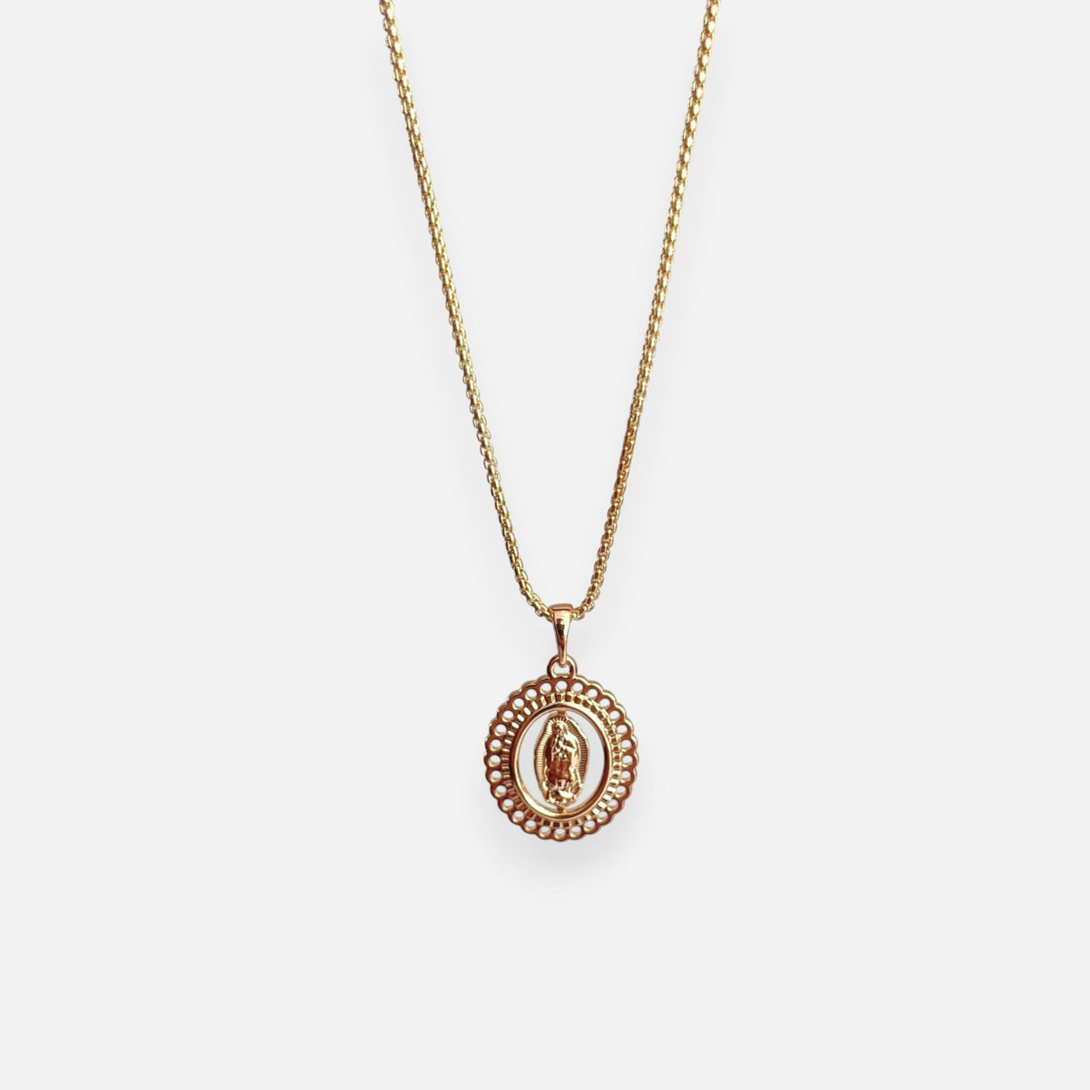 Cadena de tejido veneciana en acabado dorado, acompañada por un dije en forma de medalla ovalada con la figura central en relieve de la Virgen de Guadalupe. La pieza destaca por su elegante borde exterior calado con detalles troquelados en forma de encaje o filigrana.