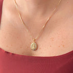 Cadena fina de tejido Veneciana en tono dorado con un dije en forma de medalla ovalada. Presenta la imagen central de la Virgen de Guadalupe sobre un fondo radiante, rodeada por un cerco engastado en incrustaciones de circonias brillantes