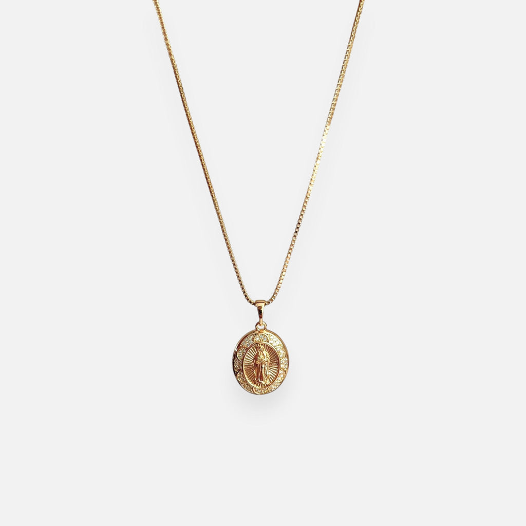 Cadena fina de tejido Veneciana en tono dorado con un dije en forma de medalla ovalada. Presenta la imagen central de la Virgen de Guadalupe sobre un fondo radiante, rodeada por un cerco engastado en incrustaciones de circonias brillantes