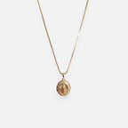 Cadena fina de tejido Veneciana en tono dorado con un dije en forma de medalla ovalada. Presenta la imagen central de la Virgen de Guadalupe sobre un fondo radiante, rodeada por un cerco engastado en incrustaciones de circonias brillantes