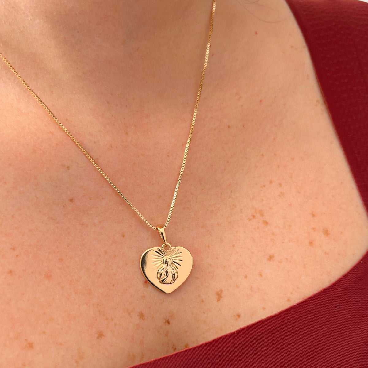 Cadena de tejido Veneciana en acabado dorado, acompañada por un dije en forma de corazón doble cara o reversible. Por una cara presenta la imagen del Sagrado Corazón de Jesús con halo radiante y por la otra la figura de la Virgen del Carmen sobre un fondo texturizado de destellos. Una pieza versátil de gran devoción y protección.