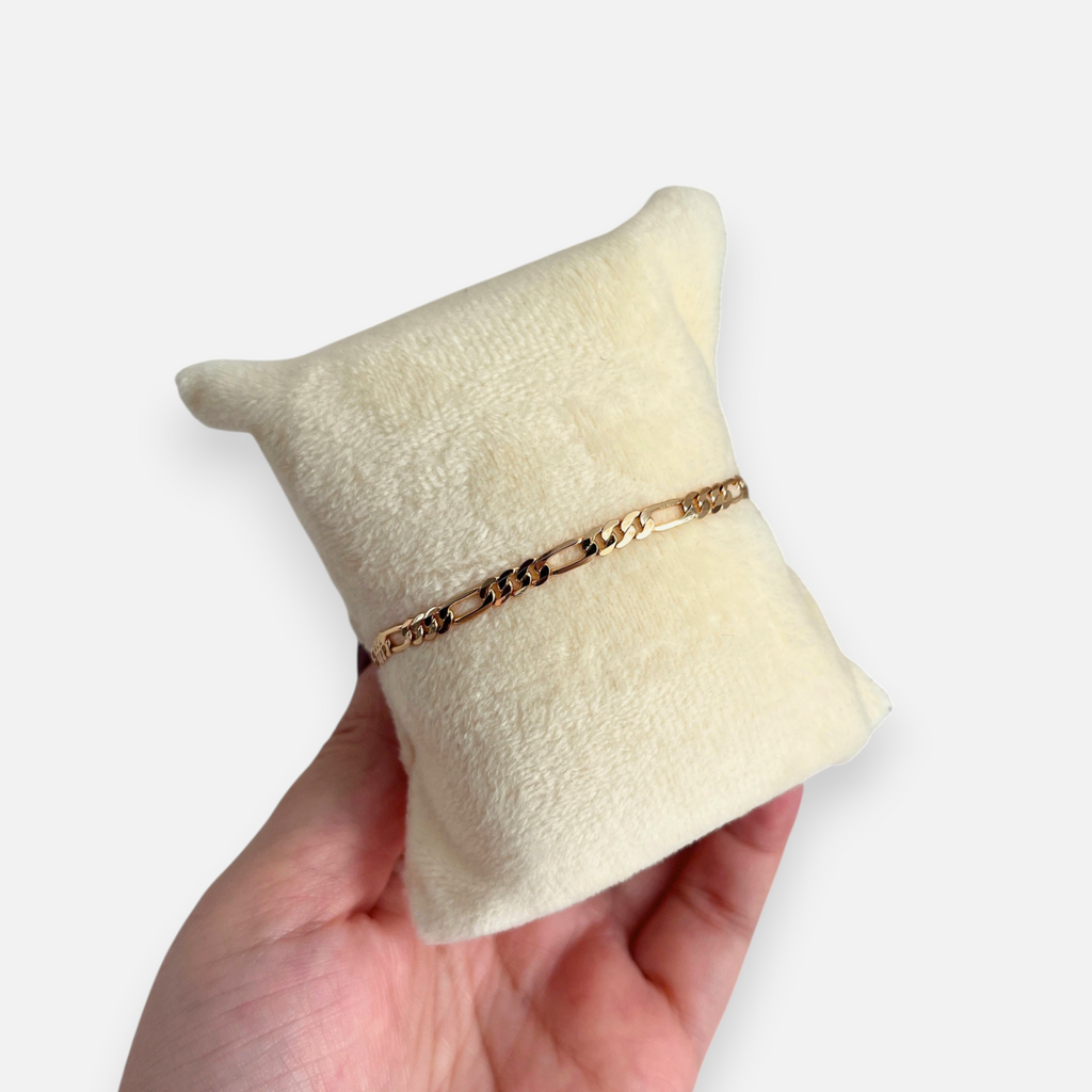 Pulsera Hv Hermanas Villegas de tejido Fígaro delgada con enchape en oro rosa sobre un cojín de exhibición beige.