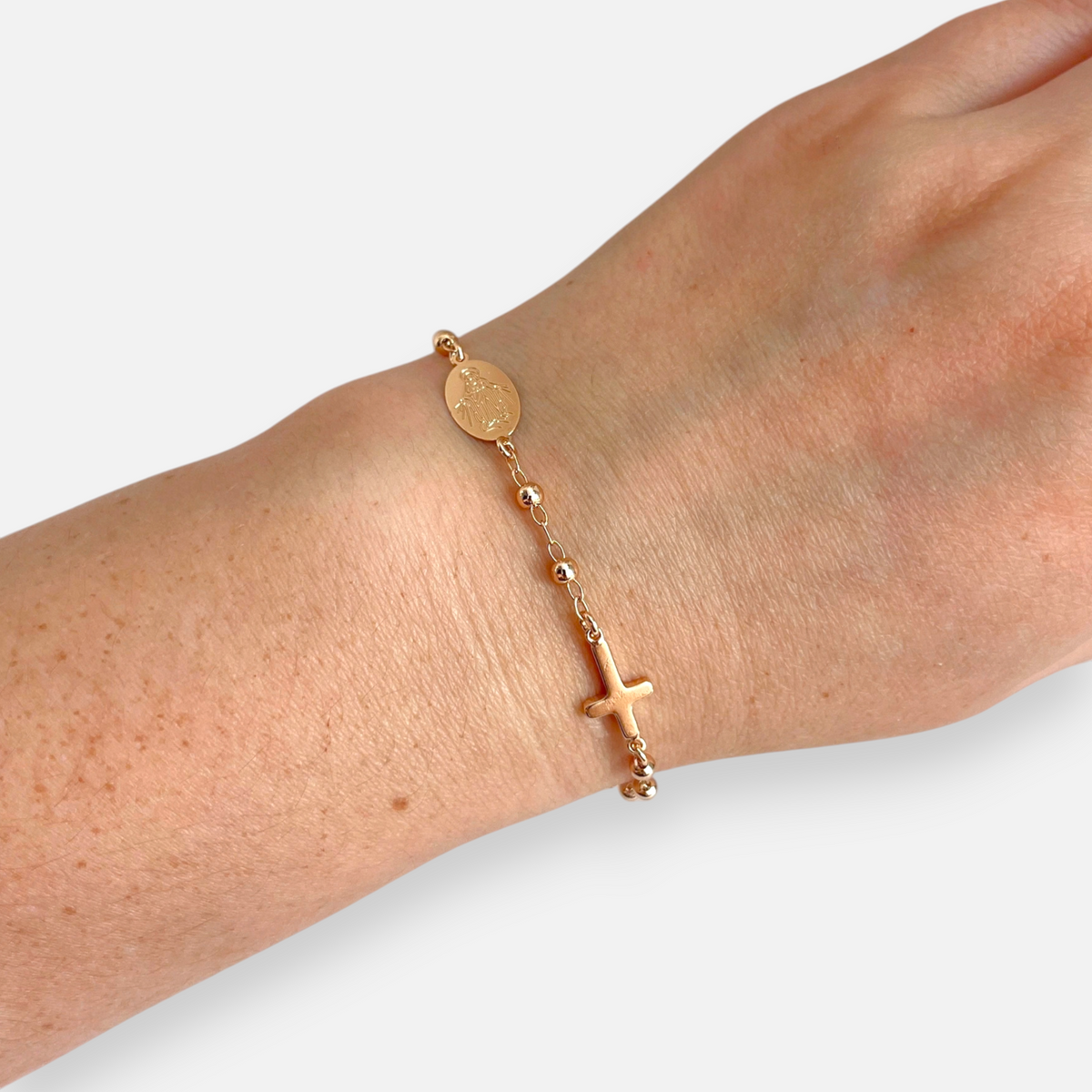 Pulsera tipo denario Hv Hermanas Villegas en oro rosé con cruz, medalla de la Virgen Milagrosa y balines brillantes.