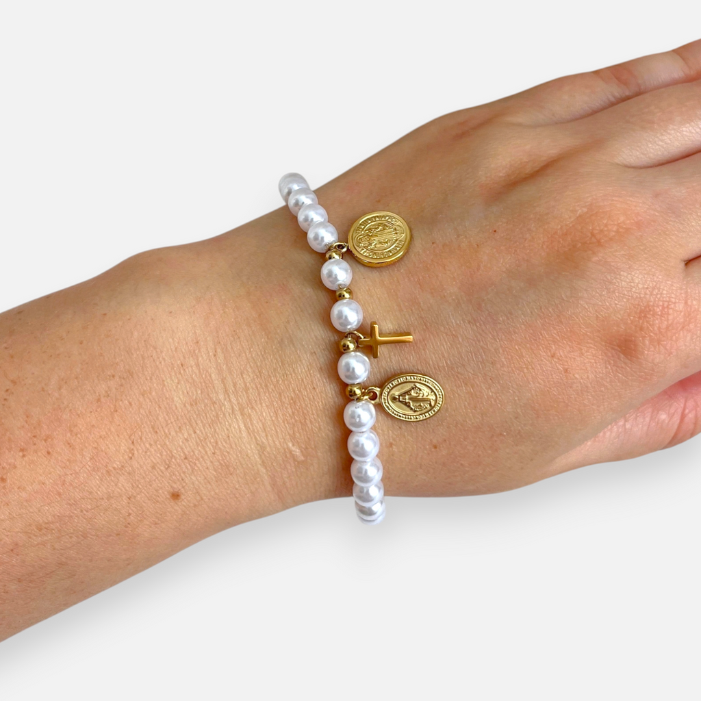 Pulsera Hv Hermanas Villegas de perlas blancas con cruz y medallas religiosas en baño de oro rosé sobre mano