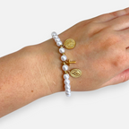 Pulsera Hv Hermanas Villegas de perlas blancas con cruz y medallas religiosas en baño de oro rosé sobre mano