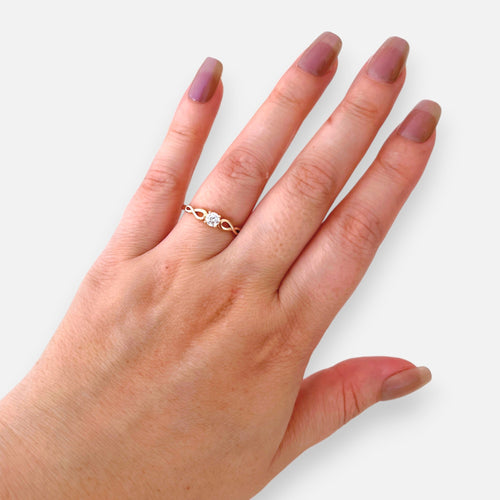 Anillo solitario Hv Hermanas Villegas en oro rosé con circonia central y banda de diseño infinito en mano femenina