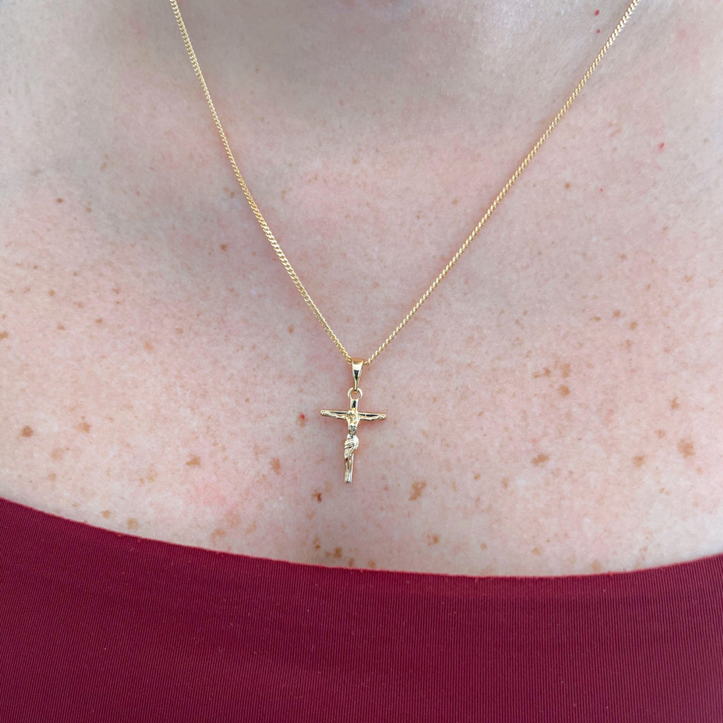 Collar Hv Hermanas Villegas con cadena grumet y dije de crucifijo estilizado en baño de oro rosé sobre el cuello.