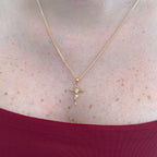 Collar Hv Hermanas Villegas con cadena grumet y dije de crucifijo estilizado en baño de oro rosé sobre el cuello.
