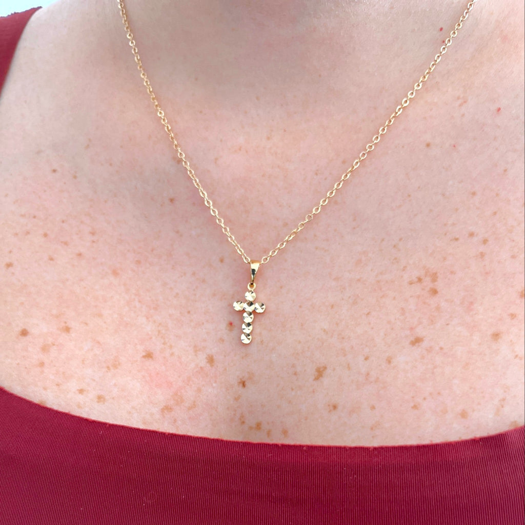 Collar Hv Hermanas Villegas con cadena forcet y dije de cruz facetada en baño de oro rosé sobre cuello femenino.