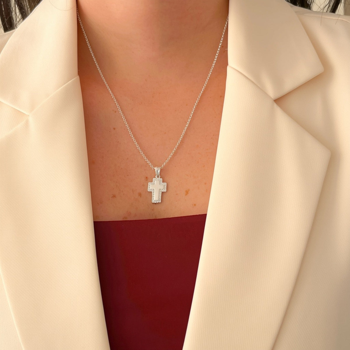 Collar Hv Hermanas Villegas de plata 925 con dije de cruz pulida y borde de circonias brillantes sobre blazer crema