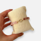 Pulsera Hv Hermanas Villegas de cuarzo rosa con dije de corazón y circones en acero dorado sobre soporte de terciopelo