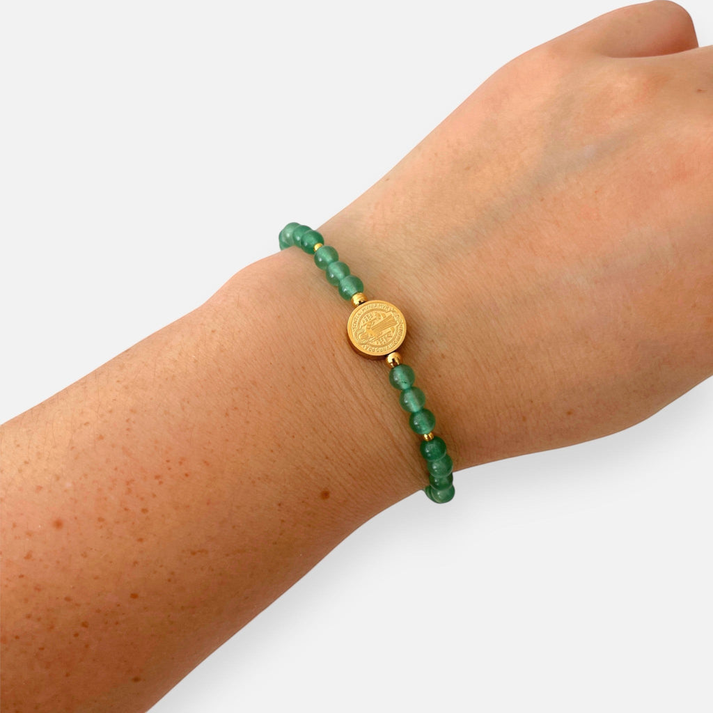 Pulsera Hv Hermanas Villegas de cuarzo verde y medalla de San Benito en acero dorado sobre muñeca femenina