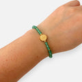 Pulsera Hv Hermanas Villegas de cuarzo verde y medalla de San Benito en acero dorado sobre muñeca femenina