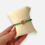 Pulsera Hv Hermanas Villegas de cuarzo verde natural y medalla de San Benito en acero dorado sobre cojín de terciopelo