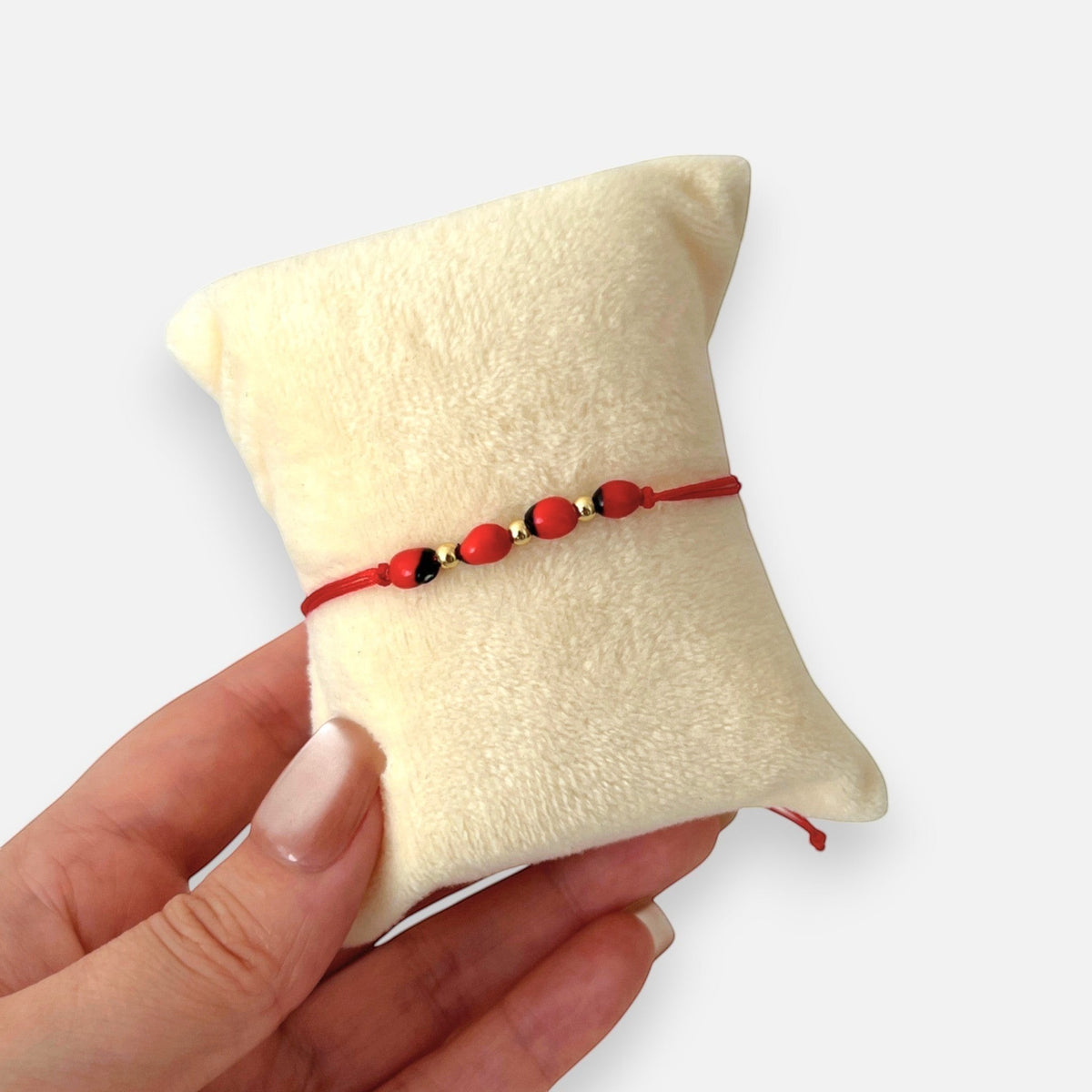 Pulsera Hv Hermanas Villegas de hilo rojo con semillas de huayruro y balines de acero dorado sobre cojín protector