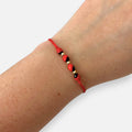 Pulsera Hv Hermanas Villegas de hilo rojo con semillas de huayruro y balines de acero dorado en muñeca