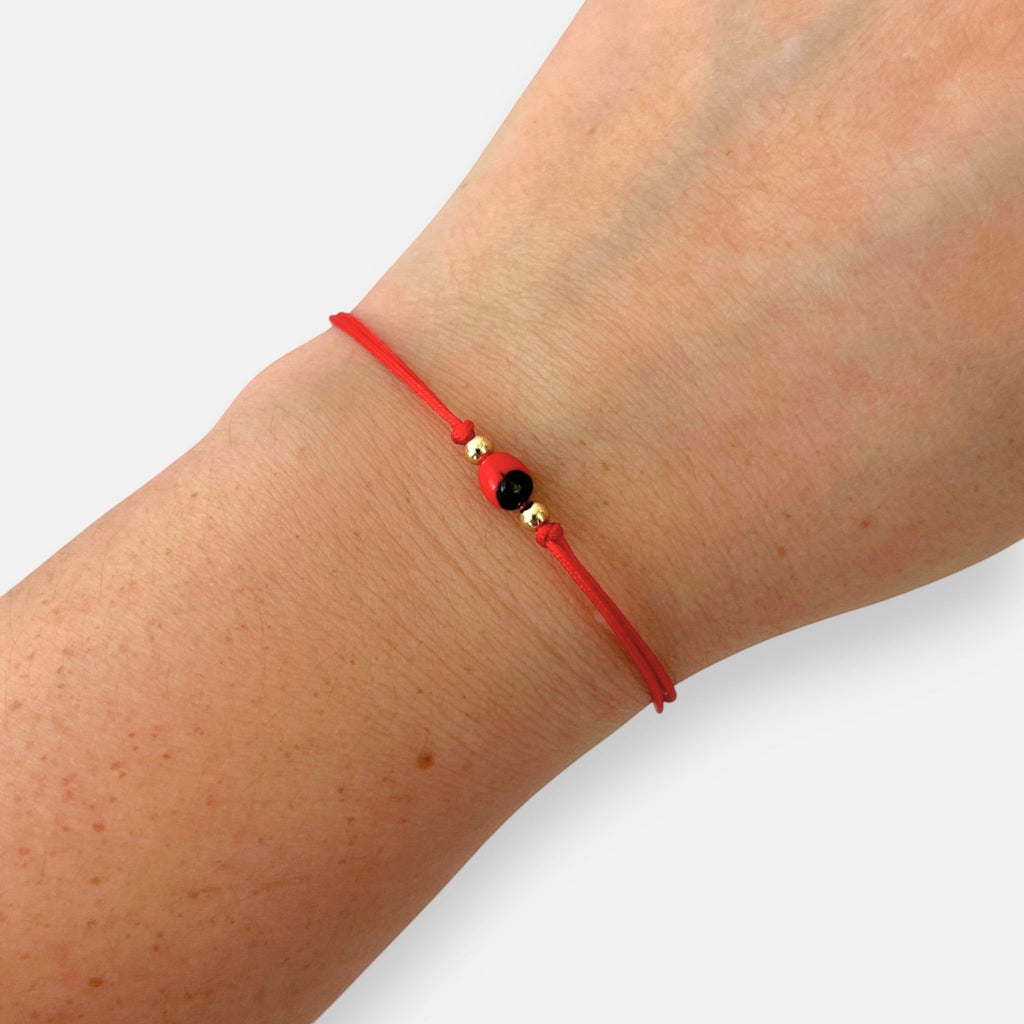 Pulsera Hv Hermanas Villegas de hilo rojo ajustable con semilla de huayruro y balines de acero dorado