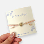 Pulsera Hv Hermanas Villegas de hilo con cuentas Murano rosa, dije San Benito en acero dorado y circones brillantes.