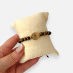 Pulsera Hv Hermanas Villegas de hilo con piedras ojo de tigre, balines y medalla de San Benito en acero dorado.