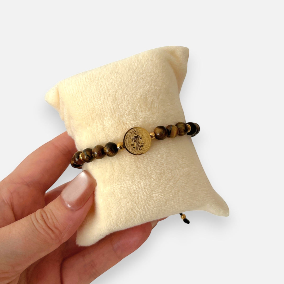 Pulsera Hv Hermanas Villegas de hilo con piedras ojo de tigre, balines y medalla de San Benito en acero dorado.