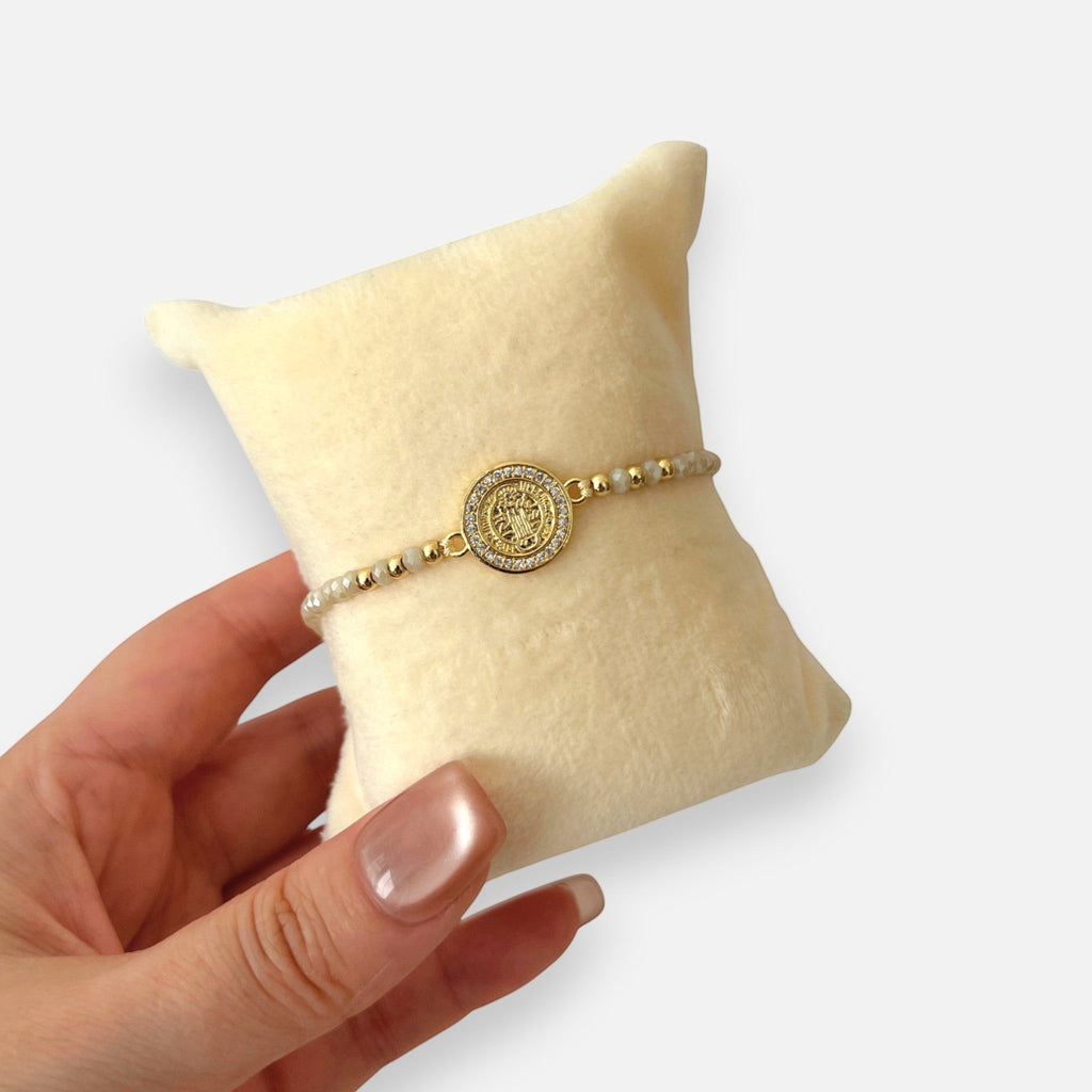 Pulsera Hv Hermanas Villegas de hilo con cuentas de Murano crema, dije de San Benito y bisel de circones dorados