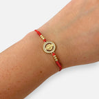 Pulsera Hv Hermanas Villegas de hilo rojo con dije de San Benito en acero dorado y circones brillantes