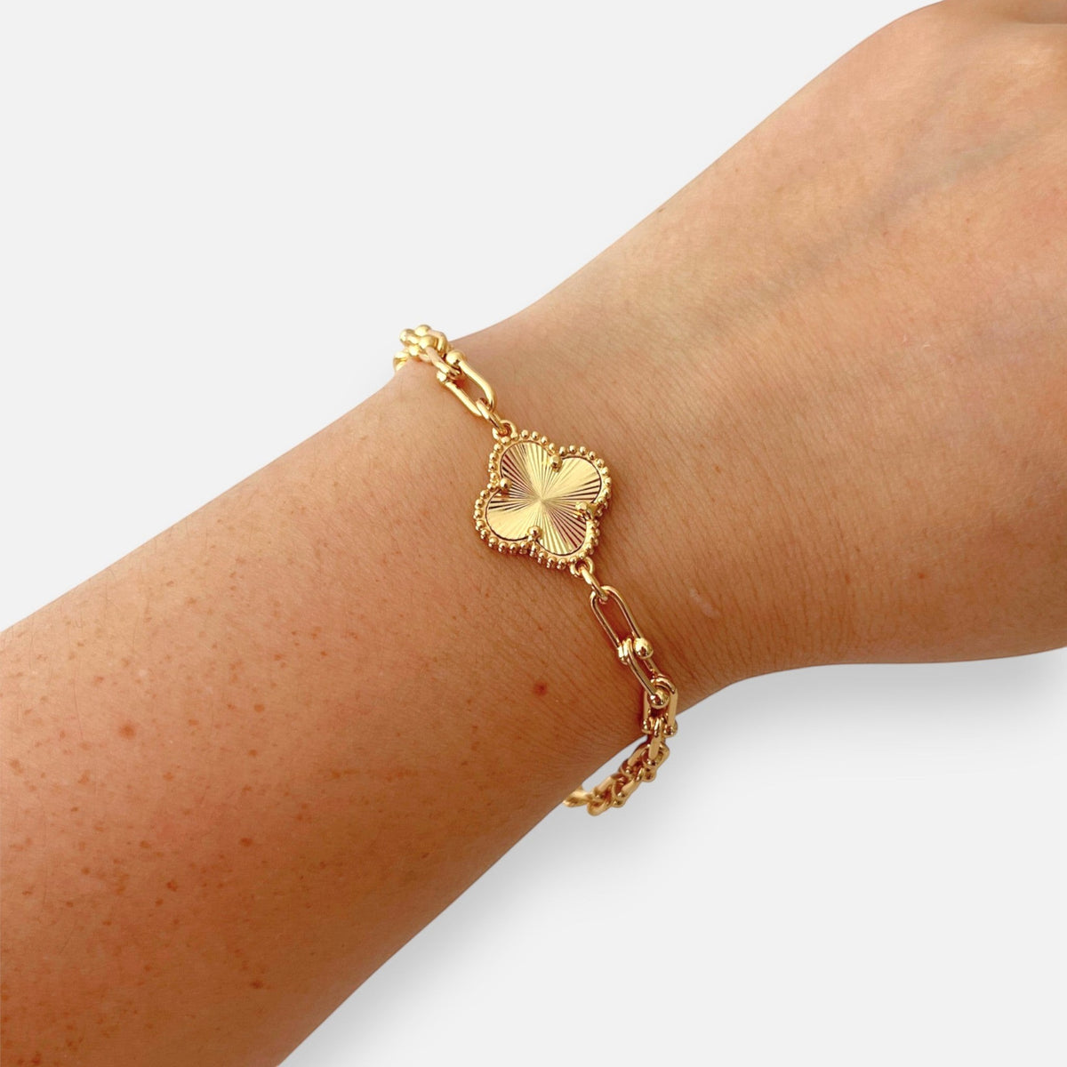 Pulsera Hv Hermanas Villegas de acero dorado con dije de trébol texturizado y cadena de eslabones tipo Tiffany