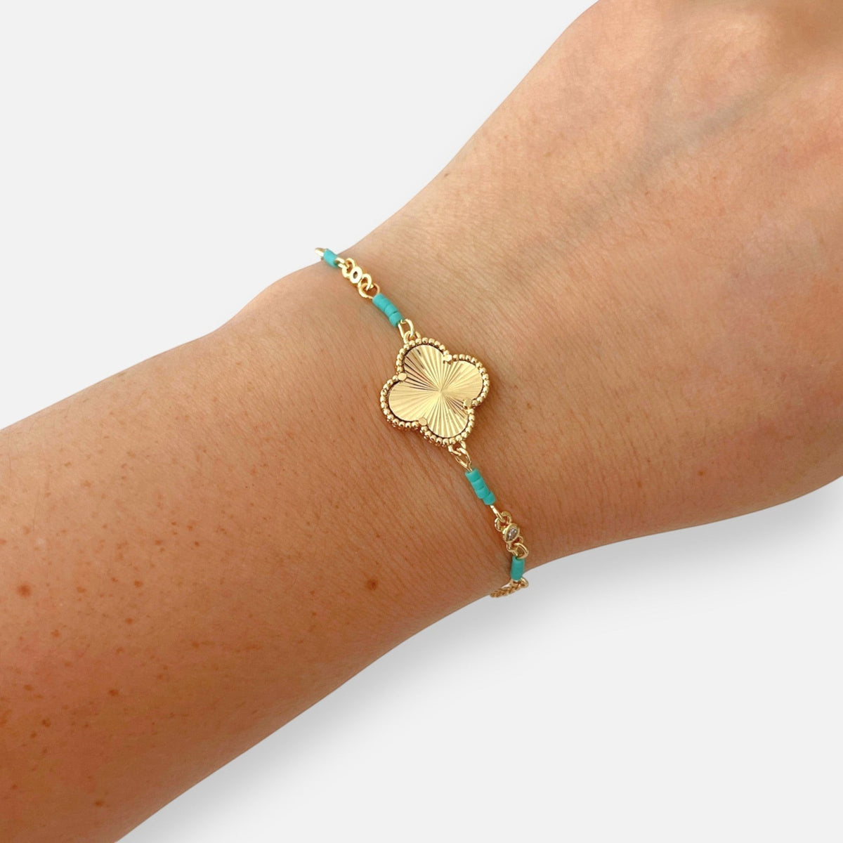 Pulsera Hv Hermanas Villegas de acero dorado con dije de trébol texturizado y cuentas turquesa