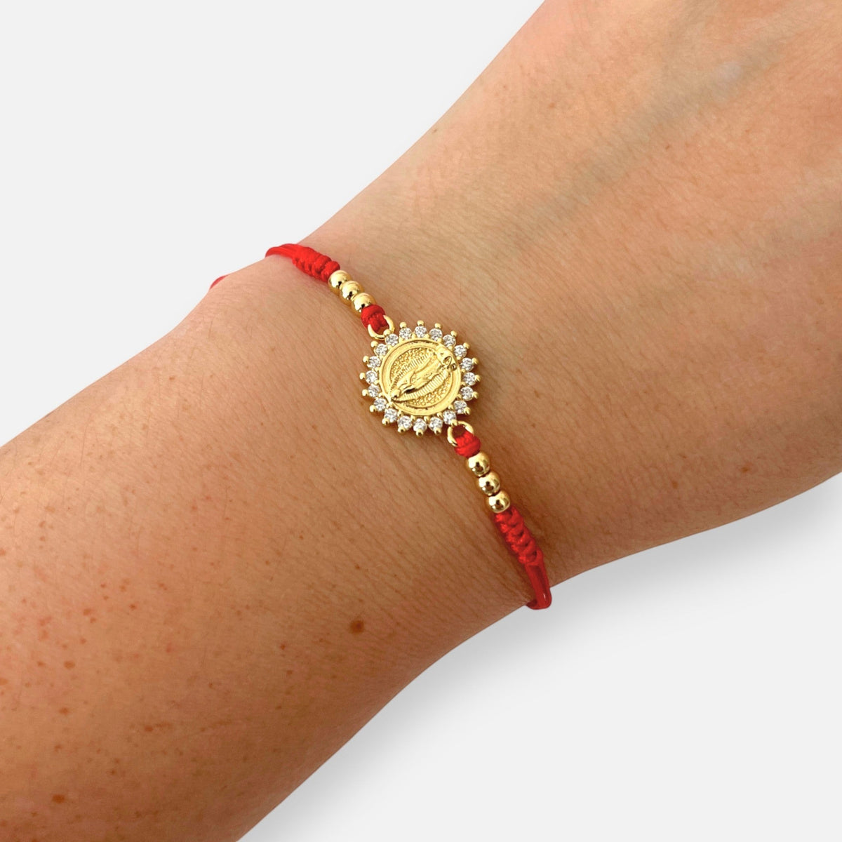 Pulsera Hv Hermanas Villegas de hilo rojo con dije de Virgen de Guadalupe, circones y balines en acero dorado.