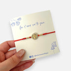 Pulsera Hv Hermanas Villegas de hilo rojo con dije de Virgen de Guadalupe, circones y detalles en acero dorado