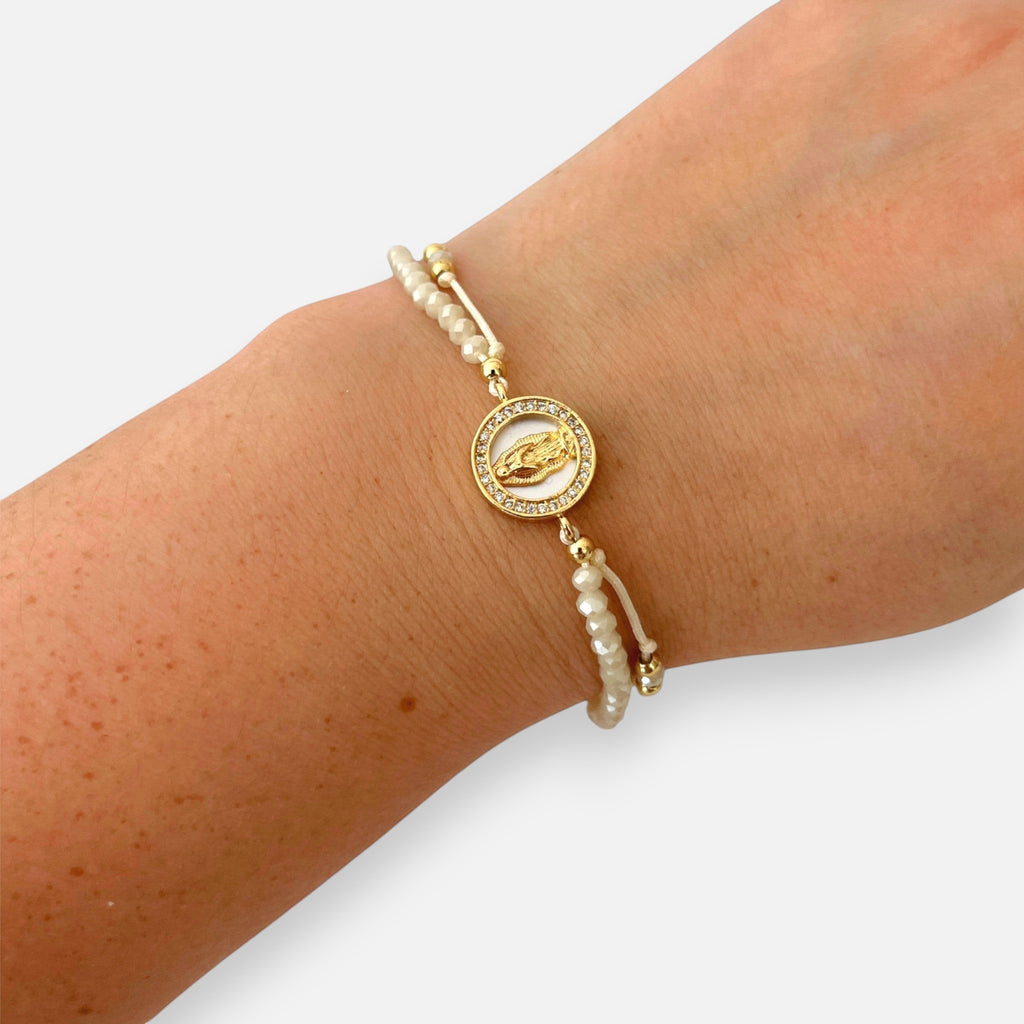 Pulsera Hv Hermanas Villegas de hilo beige con cuentas Murano, medalla Virgen de Guadalupe en nácar y acero dorado.