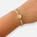 Pulsera Hv Hermanas Villegas de hilo beige con cuentas Murano, medalla Virgen de Guadalupe en nácar y acero dorado.