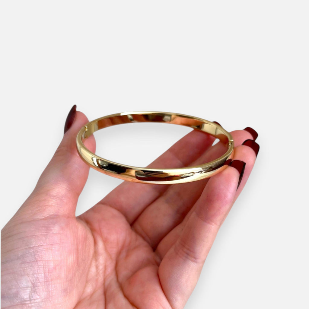 Puñera rígida Hv Hermanas Villegas en cobre con enchapado en oro, diseño liso y pulido sostenida en una mano.