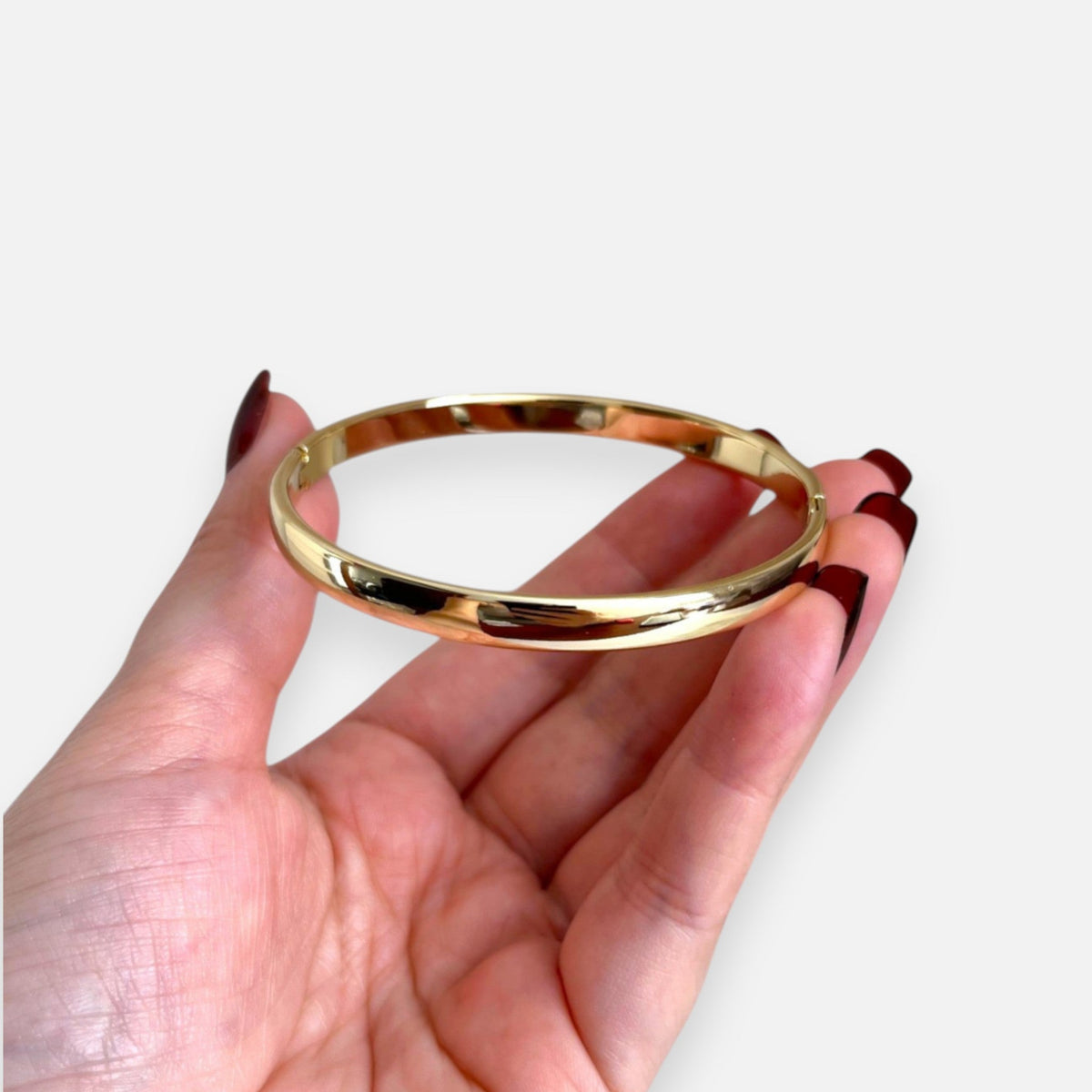 Puñera rígida Hv Hermanas Villegas en cobre con enchapado en oro, diseño liso y pulido sostenida en una mano.
