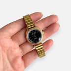 Reloj Hv Hermanas Villegas de caja cuadrada dorada, correa de eslabones y dial negro con indicadores de hora dorados.
