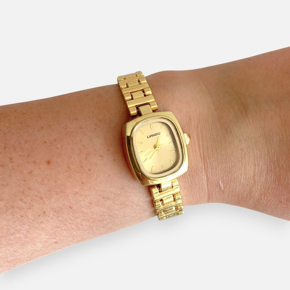 Reloj Hv Hermanas Villegas de acero dorado con caja cuadrada y correa de eslabones en una muñeca femenina