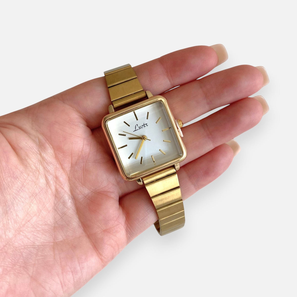 Reloj analógico Hv Hermanas Villegas con caja cuadrada dorada, dial blanco y correa metálica extensible estilo vintage.