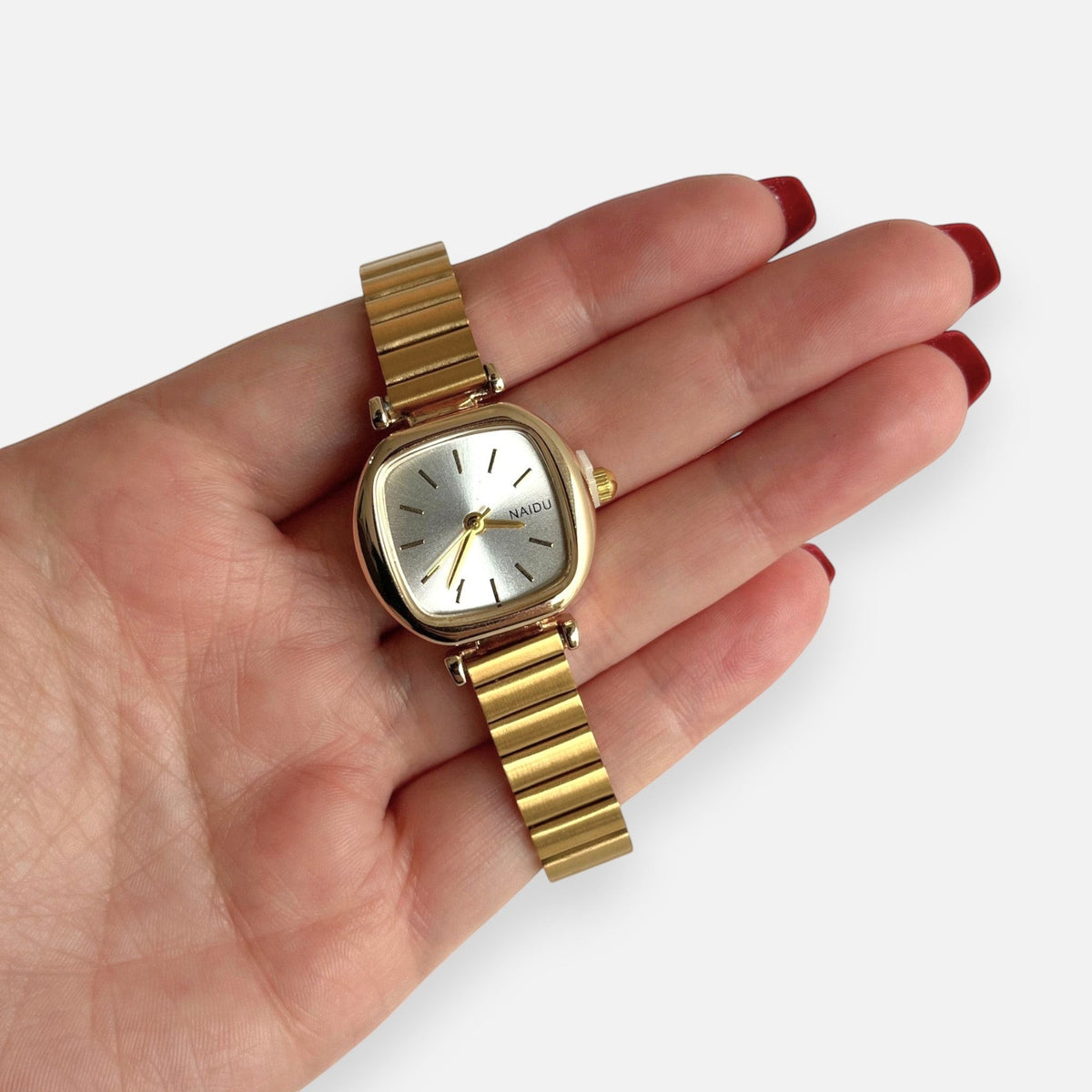 Reloj Hv Hermanas Villegas cuadrado dorado con dial champán y correa extensible flexible en mano femenina