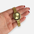 Reloj Hv Hermanas Villegas cuadrado dorado con correa de acero flexible y dial minimalista en mano femenina