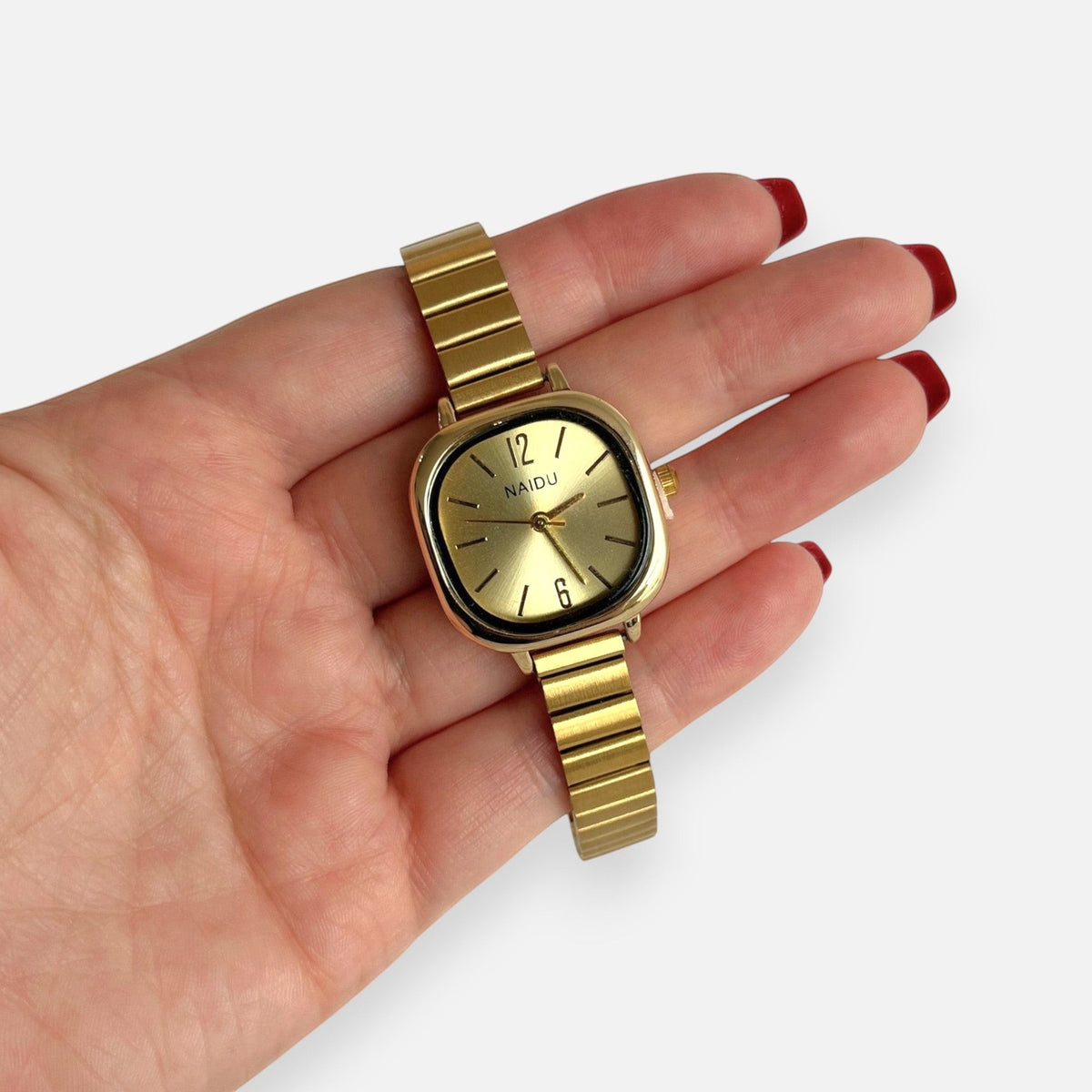 Reloj Hv Hermanas Villegas cuadrado dorado con correa de acero flexible y dial minimalista en mano femenina