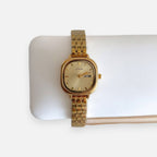 Reloj Hv Hermanas Villegas cuadrado dorado de acero con dial champaña y calendario, estilo vintage elegante.
