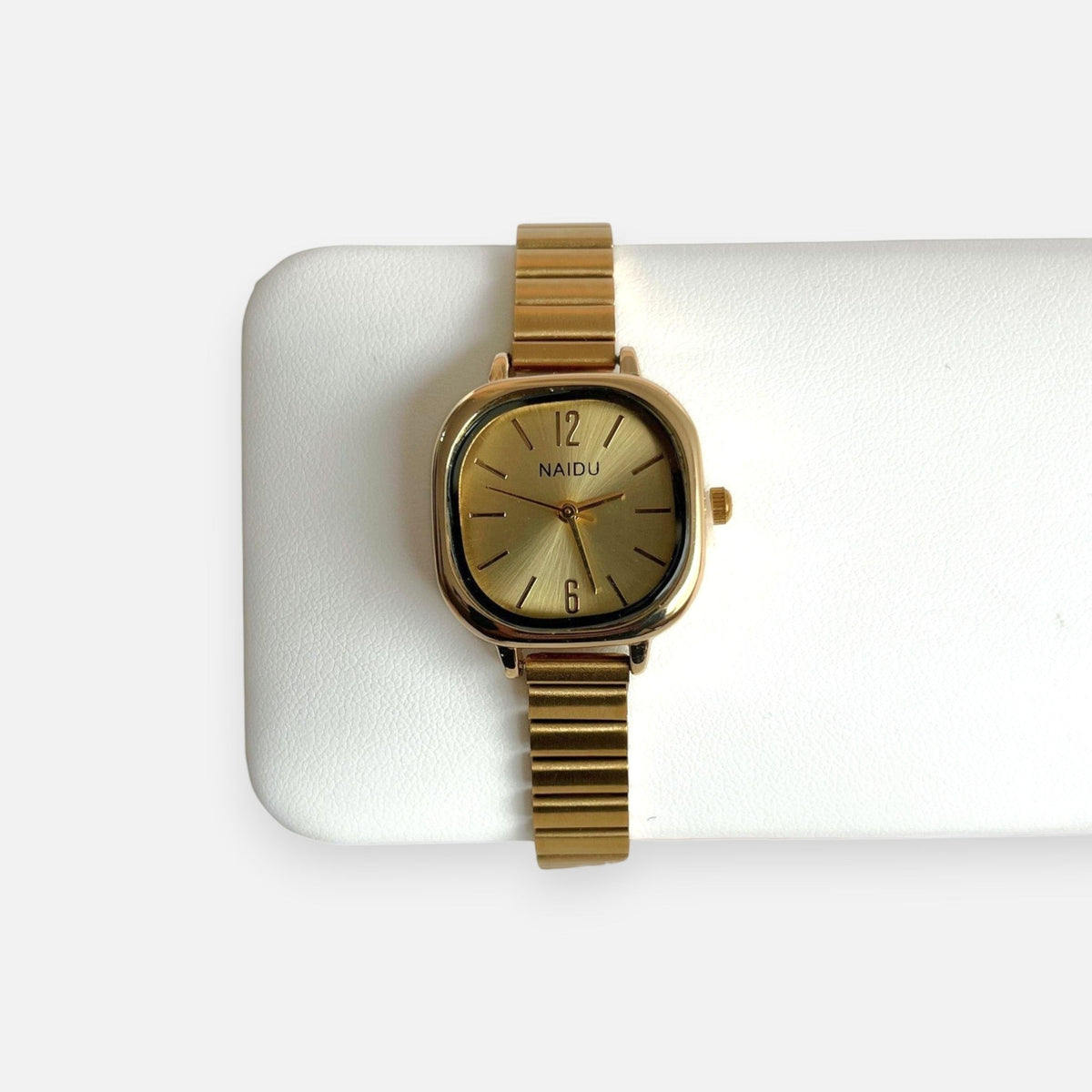 Reloj analógico Hv Hermanas Villegas con caja cuadrada dorada, dial efecto sol y correa extensible de acero flexible.