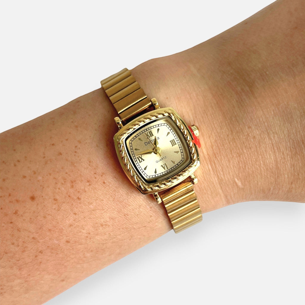 Reloj Hv Hermanas Villegas cuadrado dorado con bisel labrado, correa de eslabones y dial con números romanos.