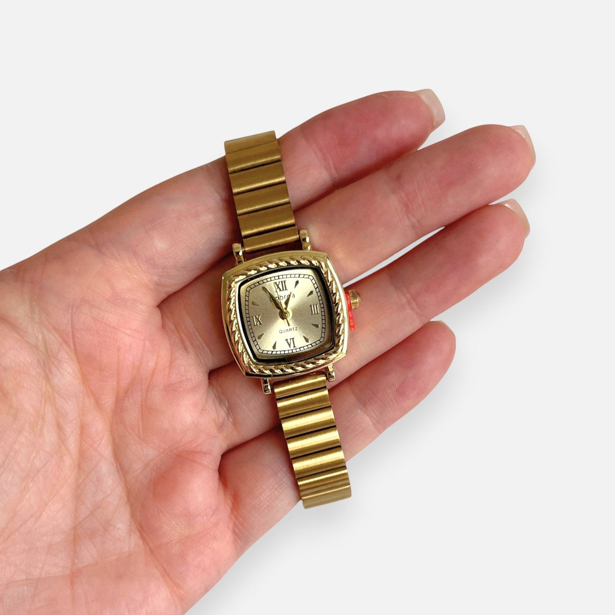 Reloj Hv Hermanas Villegas cuadrado dorado con bisel labrado, correa de eslabones y dial con números romanos.
