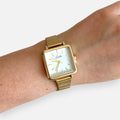 Reloj Hv Hermanas Villegas de caja cuadrada dorada, dial blanco y correa metálica extensible de estilo vintage.